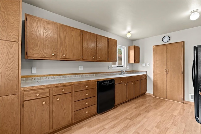 kitchen featuring black appliances, a sink, light wood-type flooring, and brown cabinetry