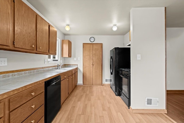 kitchen with black appliances, a sink, light wood-style floors, brown cabinets, and baseboards