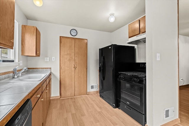 kitchen featuring black appliances, a sink, under cabinet range hood, light wood-style flooring, and brown cabinets