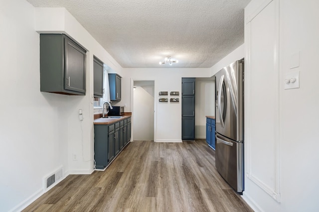 kitchen with stainless steel fridge, a sink, wood finished floors, a textured ceiling, and blue cabinets