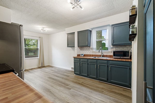kitchen with a sink, butcher block countertops, stainless steel appliances, backsplash, and a textured ceiling