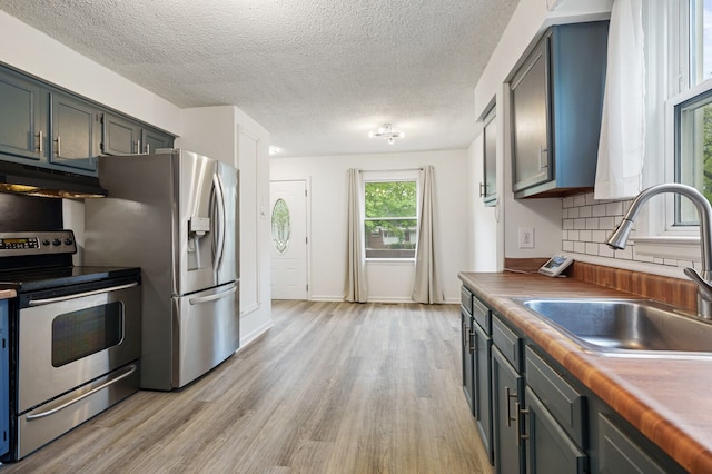 kitchen with appliances with stainless steel finishes, a sink, under cabinet range hood, light wood-style floors, and a textured ceiling