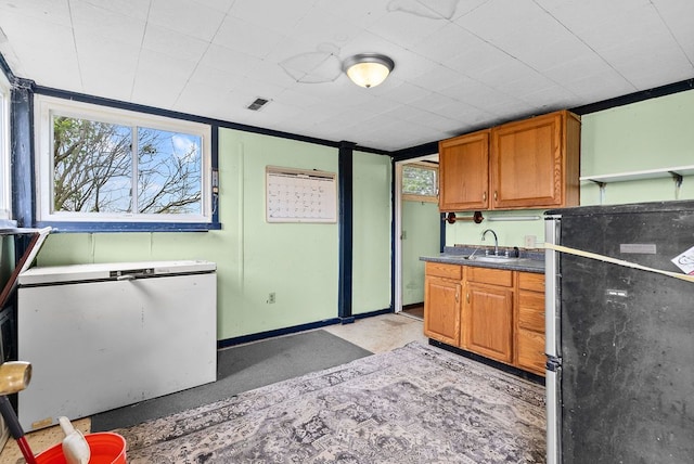 kitchen with freestanding refrigerator, brown cabinetry, a sink, and fridge