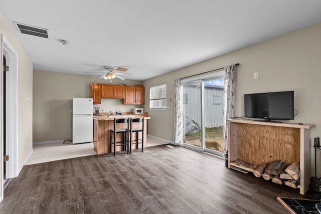 kitchen with white appliances, wood finished floors, a breakfast bar area, and baseboards