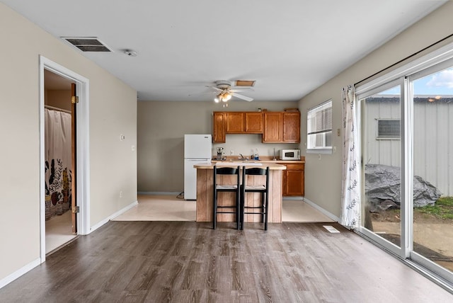 kitchen featuring white appliances, wood finished floors, brown cabinets, a ceiling fan, and light countertops
