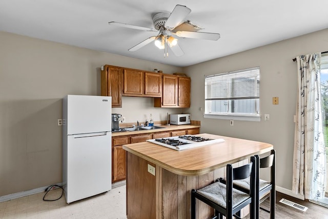 kitchen featuring white appliances, a sink, light countertops, a ceiling fan, and brown cabinets