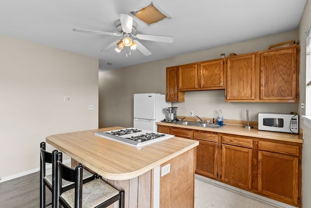 kitchen featuring white appliances, a sink, light countertops, a ceiling fan, and light flooring