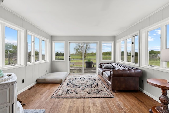 sunroom / solarium with healthy amount of natural light, hardwood / wood-style flooring, ornamental molding, baseboards, and wooden walls