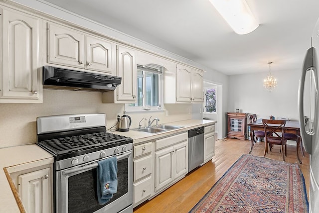 kitchen featuring appliances with stainless steel finishes, under cabinet range hood, a sink, a chandelier, and light countertops