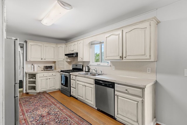 kitchen featuring appliances with stainless steel finishes, a sink, under cabinet range hood, light countertops, and light wood-style flooring