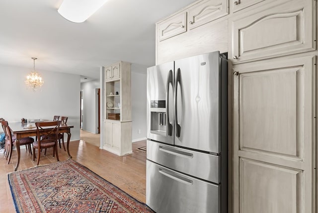 kitchen with stainless steel refrigerator with ice dispenser, a chandelier, wood finished floors, pendant lighting, and cream cabinetry