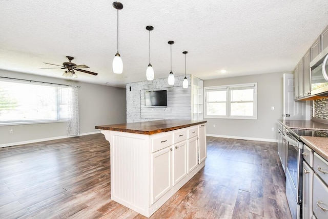 kitchen with stainless steel appliances, butcher block countertops, dark wood-style floors, plenty of natural light, and a textured ceiling