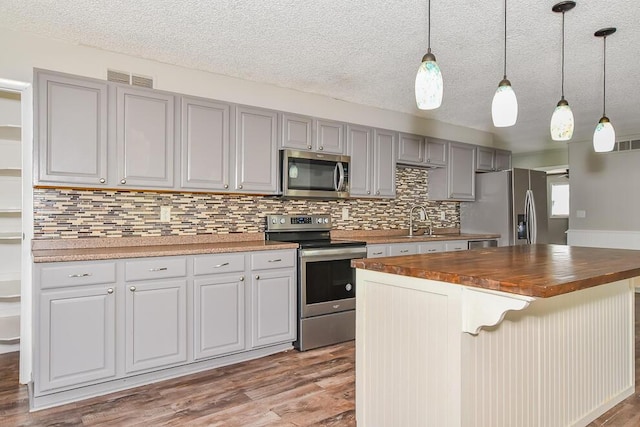 kitchen featuring appliances with stainless steel finishes, butcher block countertops, a sink, light wood-style flooring, and tasteful backsplash
