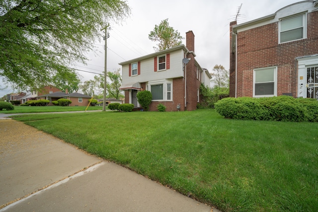 view of front of home featuring brick siding, a front yard, and a chimney