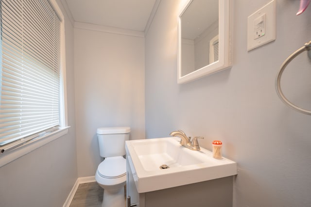 half bathroom with toilet, baseboards, ornamental molding, wood finished floors, and vanity