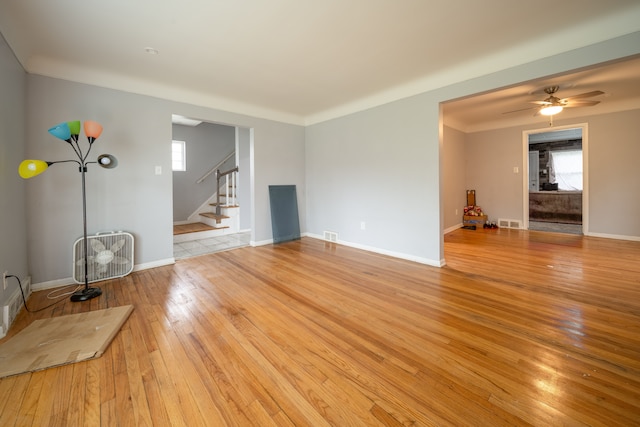 unfurnished living room featuring stairway, light wood-style floors, healthy amount of natural light, and ceiling fan