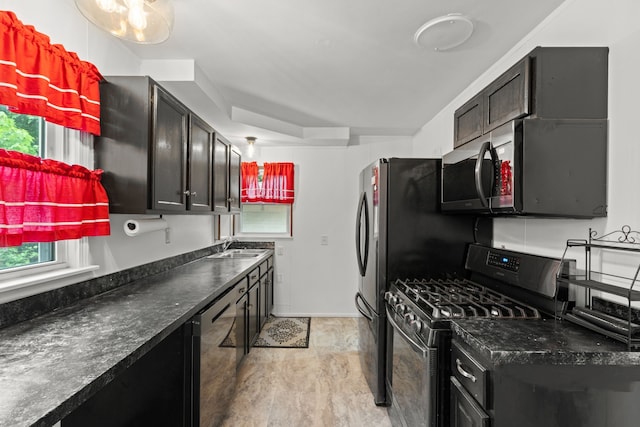 kitchen featuring stainless steel range with gas stovetop, dishwasher, dark countertops, and a sink
