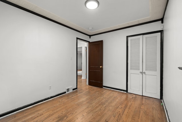 unfurnished bedroom with ornamental molding, light wood finished floors, baseboards, and a closet