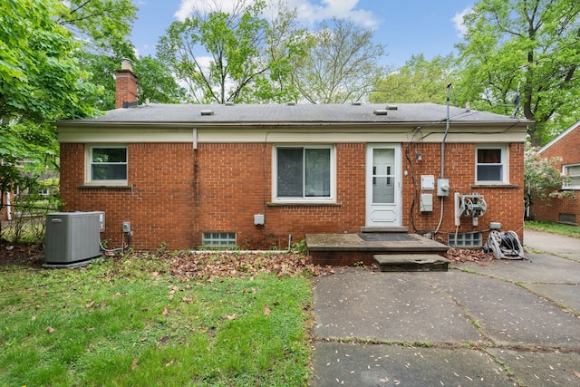 view of front facade with central AC, a chimney, and brick siding