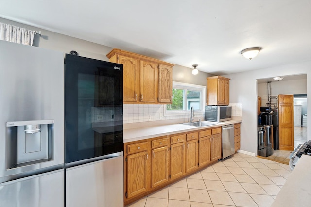 kitchen with stainless steel appliances, a sink, decorative backsplash, light countertops, and light tile patterned floors