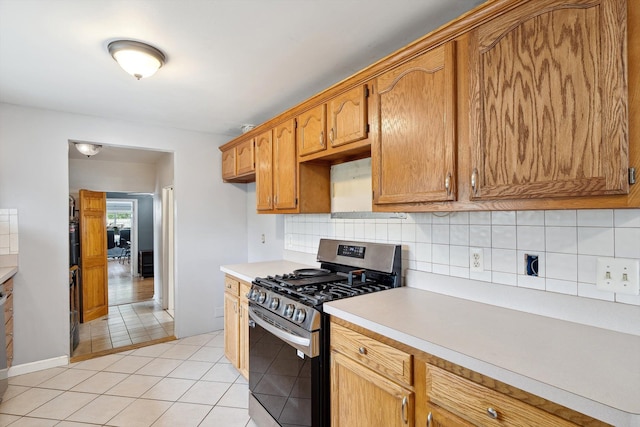 kitchen featuring gas stove, backsplash, light countertops, light tile patterned floors, and brown cabinets