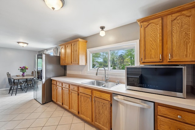 kitchen with appliances with stainless steel finishes, a sink, light countertops, light tile patterned floors, and backsplash