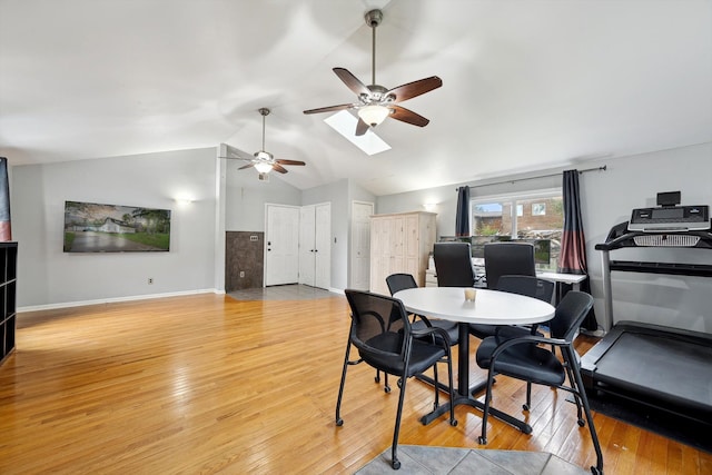 dining area with a ceiling fan, light wood-style floors, vaulted ceiling, baseboards, and a skylight