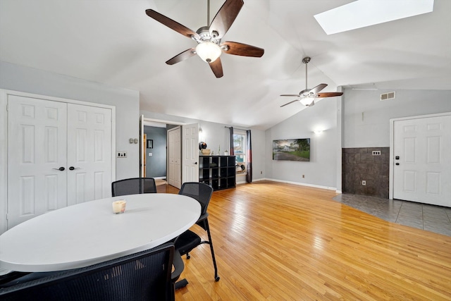 dining room with a skylight, ceiling fan, light wood-style flooring, vaulted ceiling, and baseboards