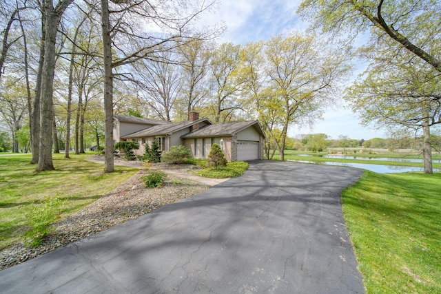 216 Wickenham Dr, Spring Arbor, MI 49283 - mid-century modern home with a water view, a chimney, a garage, asphalt driveway, and a front yard