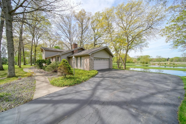 216 Wickenham Dr, Spring Arbor, MI 49283 - view of side of home featuring asphalt driveway, an attached garage, a water view, a chimney, and brick siding