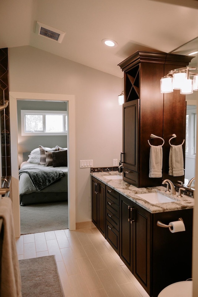 ensuite bathroom featuring double vanity, vaulted ceiling, and recessed lighting