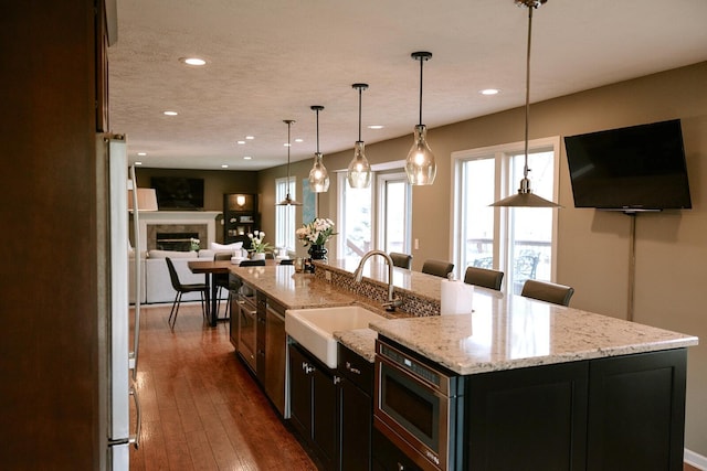 kitchen featuring a sink, stainless steel microwave, open floor plan, a large island with sink, and recessed lighting