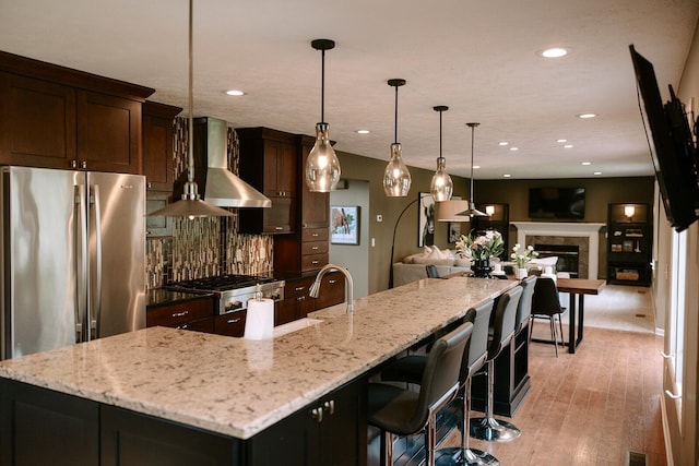 kitchen featuring wall chimney range hood, freestanding refrigerator, open floor plan, backsplash, and range