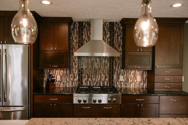 kitchen featuring stainless steel appliances, wall chimney range hood, tasteful backsplash, dark stone countertops, and dark brown cabinets