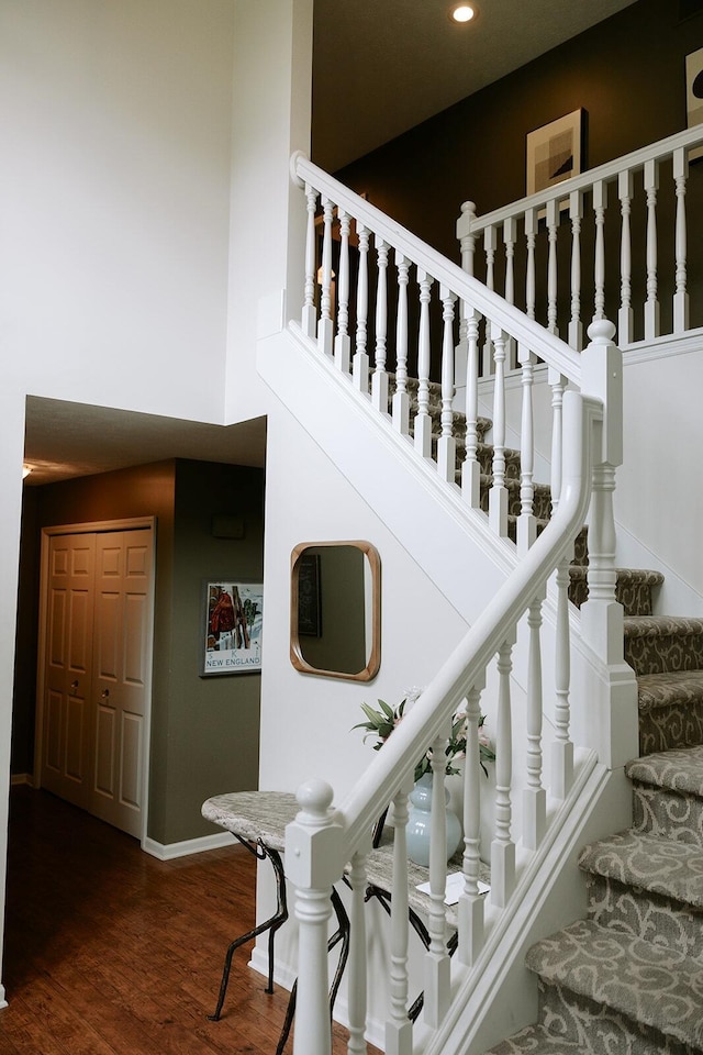 staircase featuring recessed lighting, baseboards, wood finished floors, and a towering ceiling