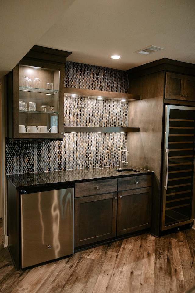 indoor wet bar featuring wine cooler, refrigerator, decorative backsplash, wood finished floors, and recessed lighting