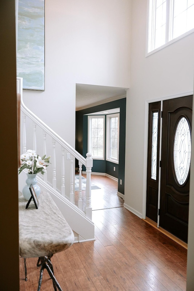foyer with plenty of natural light, a towering ceiling, stairway, wood-type flooring, and baseboards