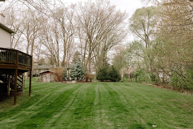 view of grassy yard with a storage shed, a deck, an outdoor structure, and stairs