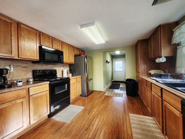 3034 Royalton Heights Rd, Saint Joseph, MI 49085 - kitchen featuring black appliances, light wood-style floors, tasteful backsplash, a textured ceiling, and brown cabinets