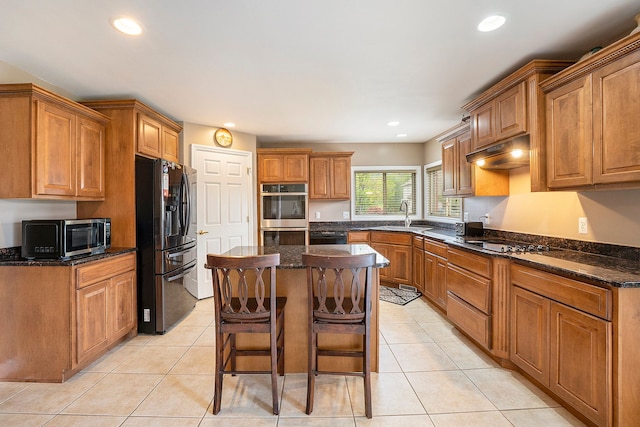 55796 Caesars Dr, Shelby Twp, MI 48315 - kitchen featuring stainless steel appliances, under cabinet range hood, a center island, brown cabinetry, and light tile patterned floors