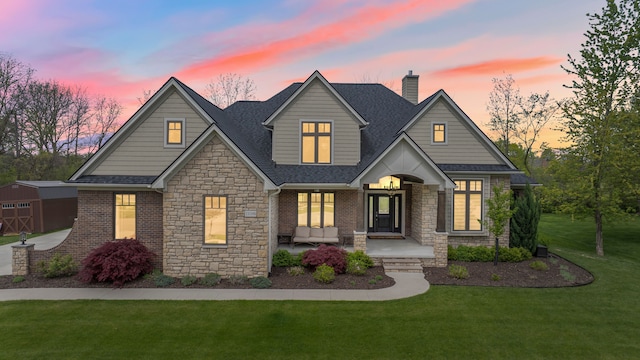 view of front of home featuring stone siding, a porch, an outbuilding, a front lawn, and roof with shingles