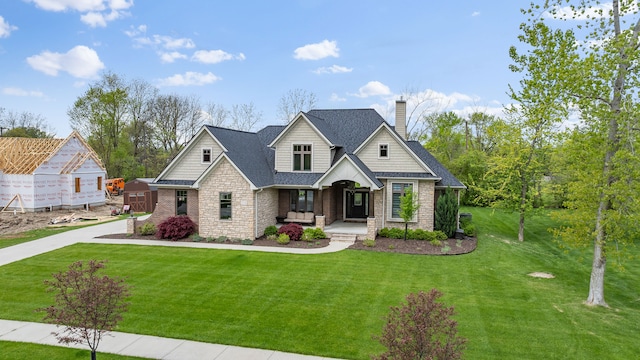 craftsman inspired home with covered porch, a chimney, stone siding, and a front yard