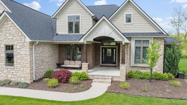 craftsman-style house with roof with shingles, stone siding, and covered porch