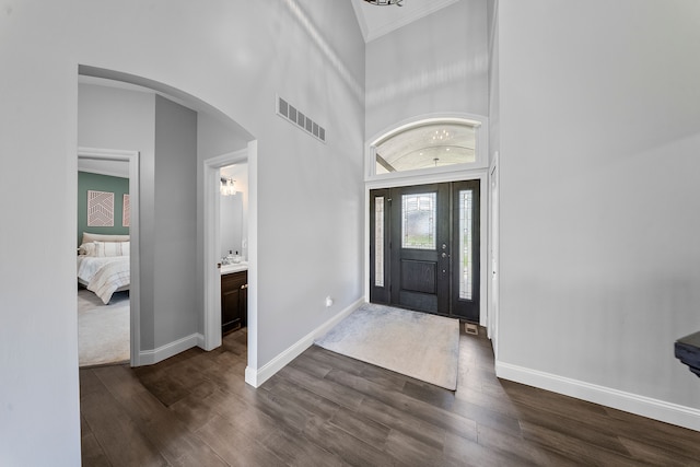 entryway with dark wood-type flooring, baseboards, arched walkways, and a high ceiling