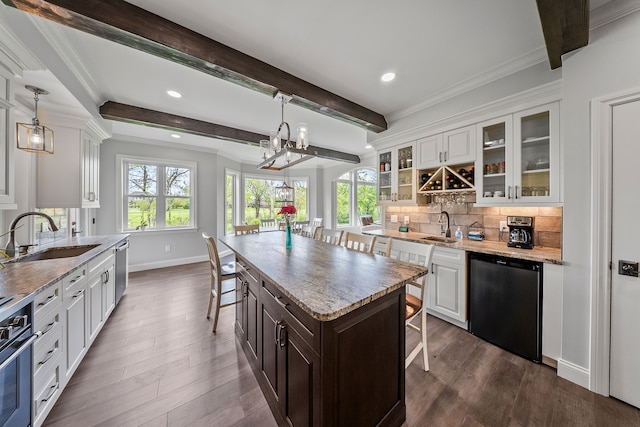 kitchen with a sink, dishwasher, a kitchen bar, white cabinets, and beam ceiling