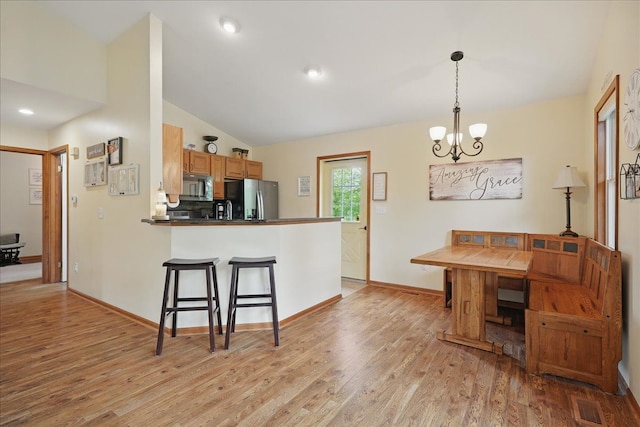 kitchen with appliances with stainless steel finishes, a chandelier, a breakfast bar area, vaulted ceiling, and light wood-type flooring