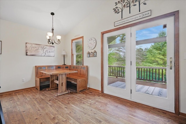 dining area featuring light wood-style flooring, a chandelier, lofted ceiling, and baseboards