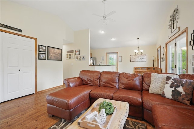 living room featuring lofted ceiling, wood finished floors, a chandelier, a ceiling fan, and baseboards