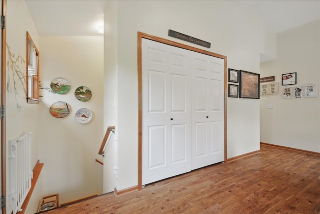 corridor with an upstairs landing, wood finished floors, and baseboards