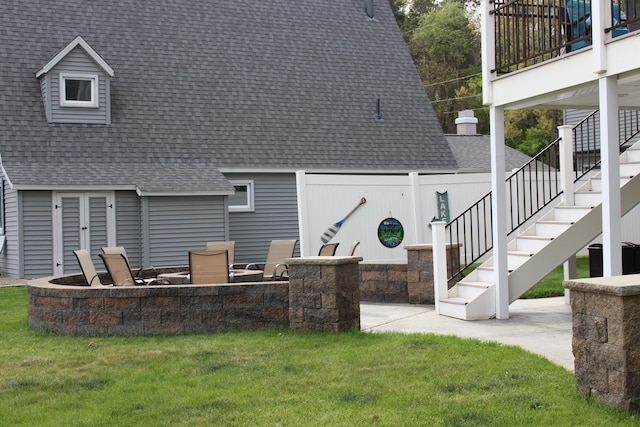 rear view of house featuring stairs, a shingled roof, a fire pit, and a lawn